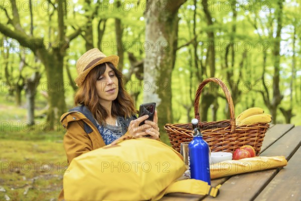 A young Caucasian mother looking at her cell phone sitting at a picnic table in the woods. Summer