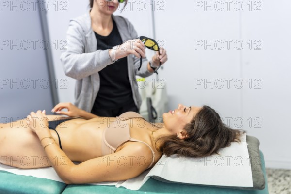Beautician putting protective glasses on a woman before starting a laser hair removal treatment