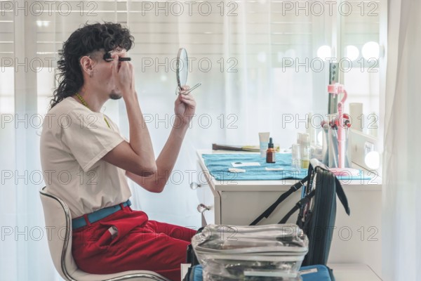 Young make-up artist applying eyebrow pencil while looking in a mirror and getting ready for a