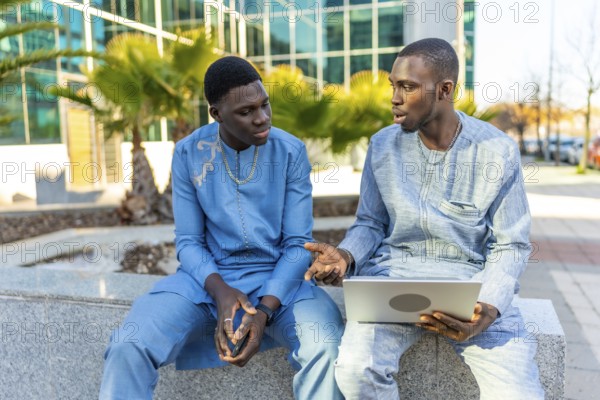 Two senegalese businessmen wearing traditional dashiki attire are sitting outside a modern office