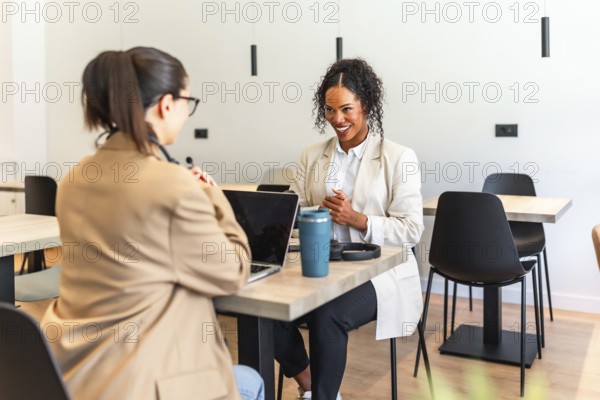 Two businesswomen are working together on a project in a modern office space, using a laptop and
