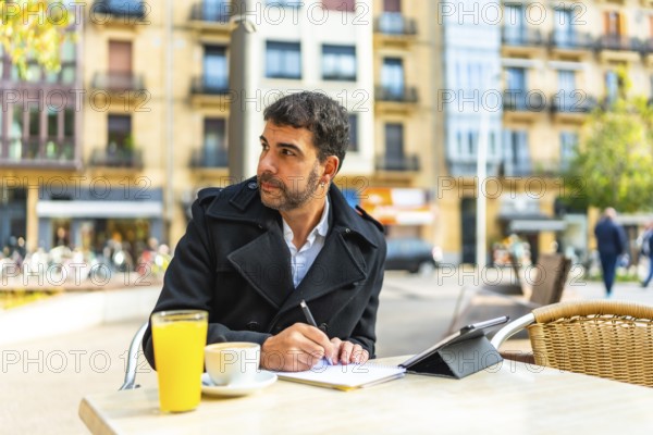 Mature handsome caucasian businessman writing notes and using digital tablet sitting on an outdoors