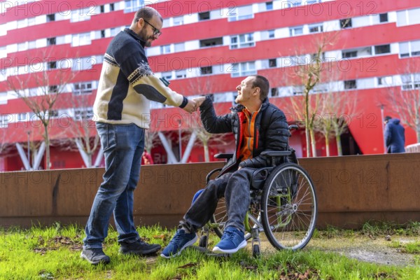 Two friends shaking hands in a city park, one of whom is using a wheelchair, demonstrating support