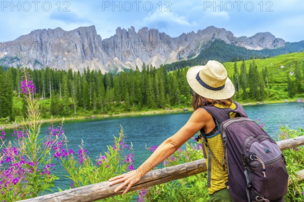 Female hiker with backpack enjoying the stunning turquoise waters of lake carezza with the latemar