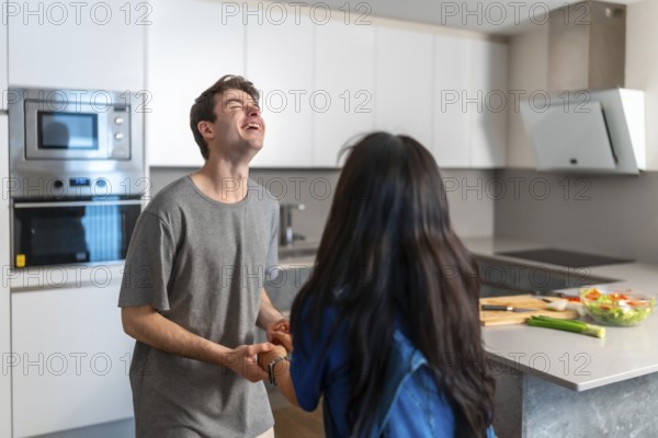 Asian woman and caucasian man sharing a joyful moment in a bright, contemporary kitchen,