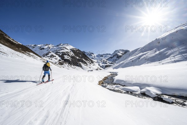 Ski tourer in the snow by a mountain stream in the Funtauna Valley, Sonnenstern, Graubünden Haute