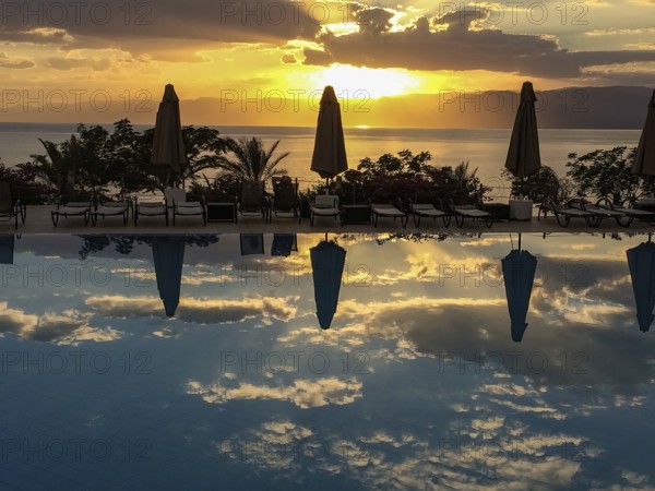 Sunset illuminated Red Sea and clouds Altostratus closed parasols reflected in swimming pool,