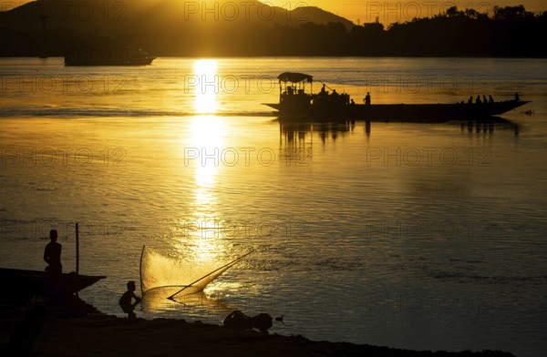 Fishermen fishing next to boats in the Brahmaputra river, during sunset in Guwahati, Assam, India
