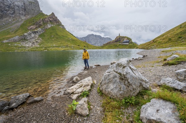 Mountaineer in yellow jacket at the mountain lake, view over the Wolayersee lake to the alpine club