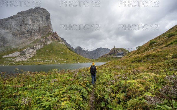 Mountaineer on hiking trail at Wolayersee, Alpine Club hut Wolayerseehütte, rocky cloudy mountains,