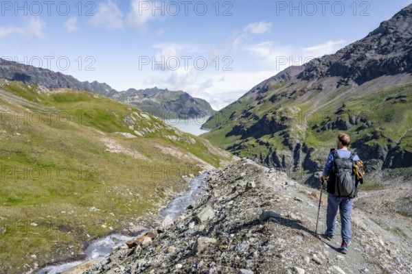Mountaineers on a hiking trail by a mountain stream, behind the Lac des Dix reservoir, Valais Alps,