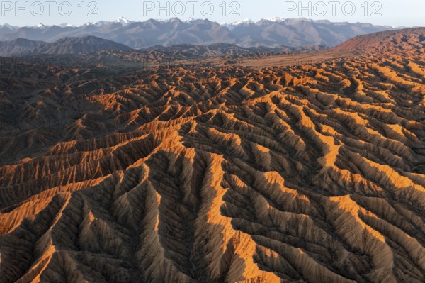 Landscape of eroded hills, badlands at sunset, mountain peaks of the Tian Shan Mountains in the