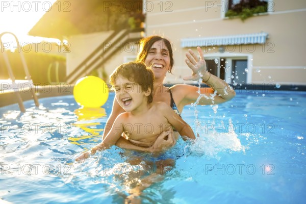 Happy mother and son are having fun, splashing and playing in a swimming pool during summer