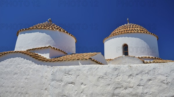Two white painted church towers with red tiled roofs and small windows, bright blue sky, Chora, Old