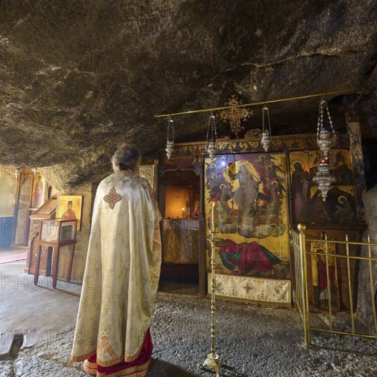 A clergyman stands in front of a scenic decorated room in a church during a service, rock grotto,