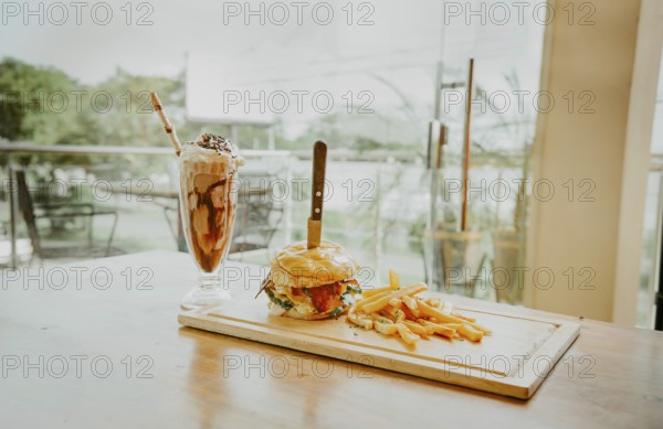 Close up of burger with fries and milkshake on wooden board with space for text. Delicious big
