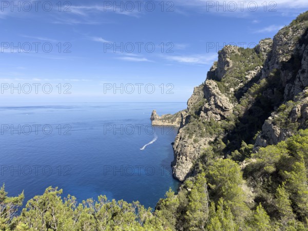 Rugged cliffs overlooking the deep blue sea, crossed by a boat on the water, Cala d'en Sardina,