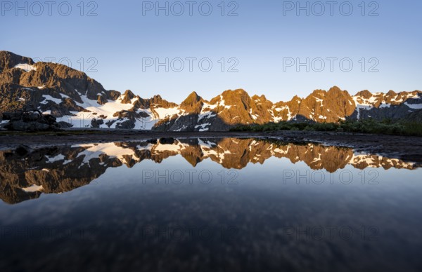 Rocky mountain peaks reflected in a small pond, mountain landscape with alpenglow at sunrise, at