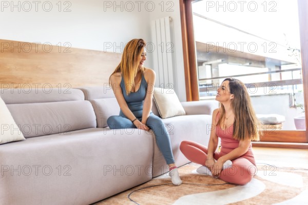 Two smiling female friends in sportswear chatting and relaxing after practicing yoga together in