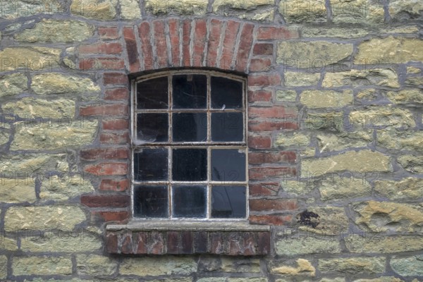Single window embedded in a masonry stone wall with brick frame in an old farmhouse, North