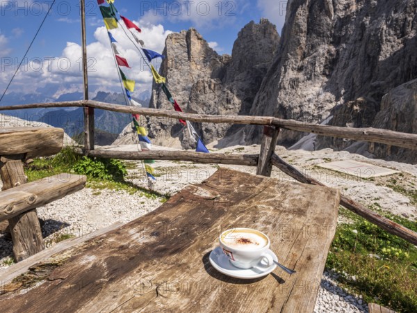 A cup of cappuccino, tibetian flag of prayer, mountain hut Rifugio Mulaz, Pala mountain group in