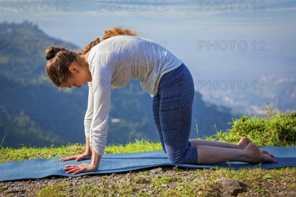 Yoga exercise outdoors, sporty fit woman practices yoga asana Marjariasana, cat pose outdoors in