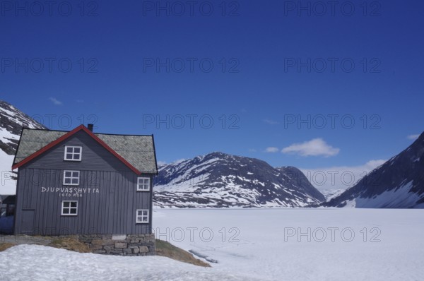 Mountain hut in a snow-covered late winter landscape, surrounded by mountains and a frozen lake,
