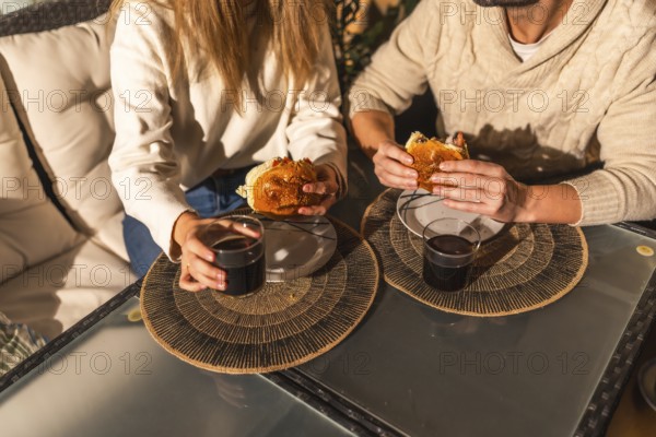 Couple sharing a relaxed moment, eating burgers and drinking beverages at a glass table, creating a