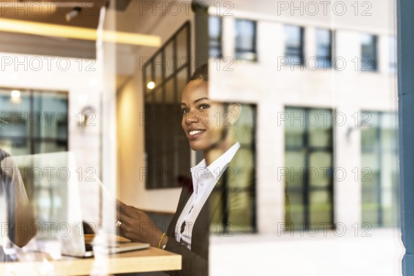 Views from outside the window of a distracted businesswoman using mobile phone working in a modern