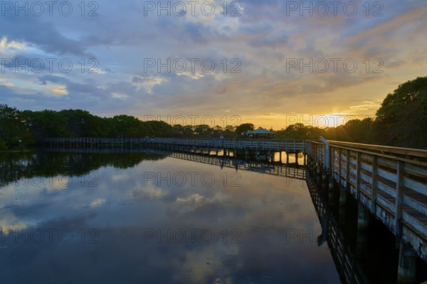 Peaceful lake reflecting the sky at sunset with a wooden bridge stretching across, surrounded by