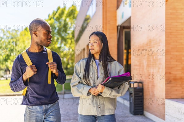 Two african and chinese multi-ethnic friends talking walking along university campus carrying