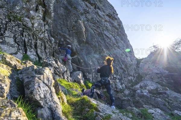 Two female rock climbers scaling a steep cliff face, illuminated by bright sunlight, showcasing