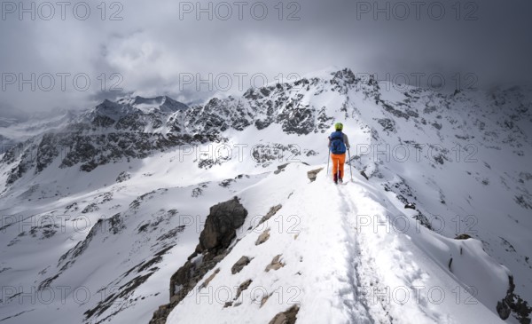 Mountaineer descending the narrow ridge of Piz Laviner, view of mountain panorama in wintry
