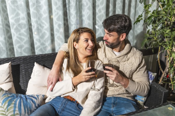 Romantic couple enjoying a glass of wine together, embracing on a comfortable sofa on their terrace