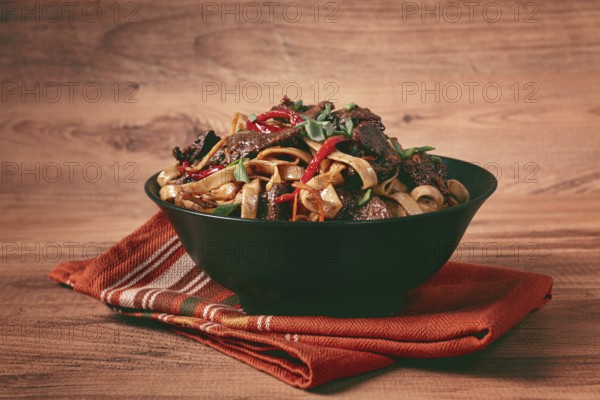 Udon noodles with beef in Mongolian style, with green onions and vegetables, served in a black