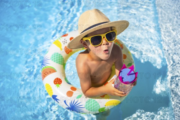 Top view of an expressive caucasian boy wearing sunglasses and sun hat playing inside a pool with
