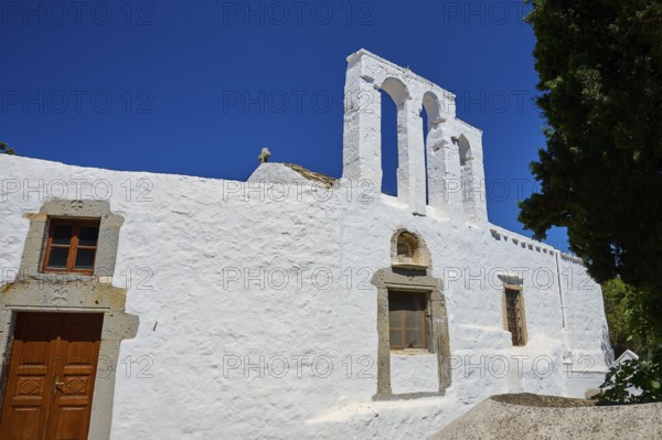 White church with bell tower and wooden door in front of a bright blue sky, Chora, Old Town,