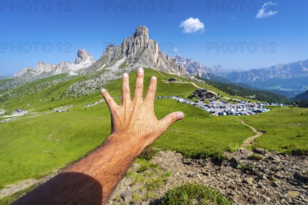 Male tourist showing five fingers with the majestic nuvolau peak and the passo giau mountain pass