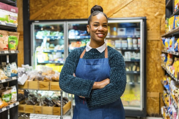 Smiling young african american saleswoman wearing an apron, standing confidently with arms crossed