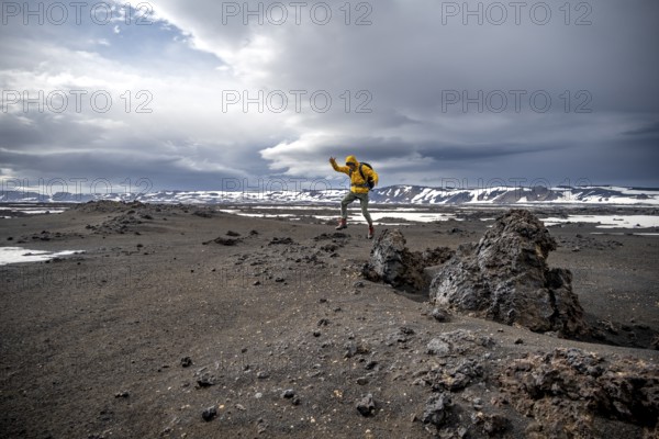 Hiker jumps into the air, snow-covered volcanic landscape with volcanic sand and petrified lava,