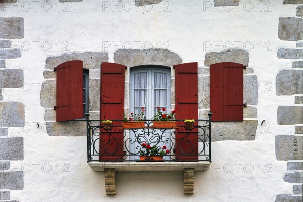 Typical window with balcony, red shutters and potted plants, detail of the façade, Espelette,