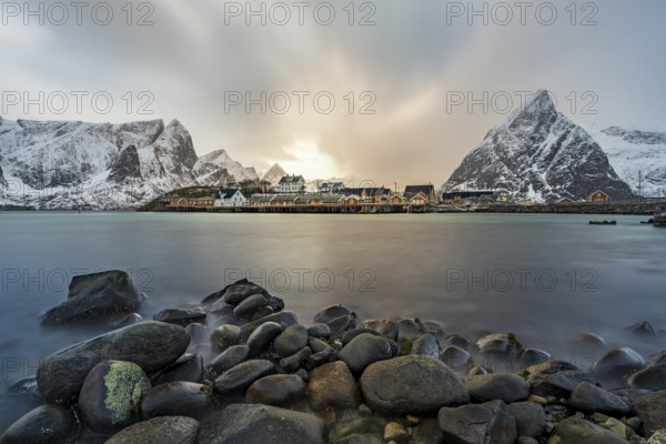 Traditional yellow rorbuer cabins on Sakrisøy Island, snow-capped rocky mountains in the back,