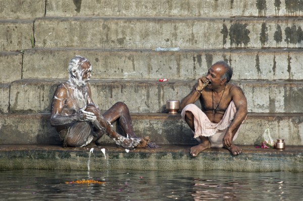 Indian men washing with soap and cleaning teeth at a ghat along the holy Ganges river, Varanasi,