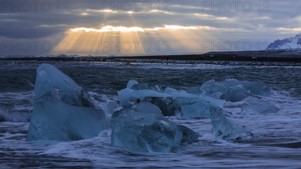 Waves breaking on icebergs on the black beach of Breidamerkursandur, sunset, near Jökullsarlon,