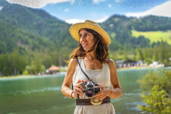 Woman wearing straw hat holding vintage camera enjoying breathtaking view of lake dobbiaco and