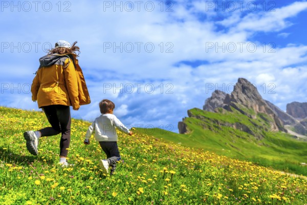 Tourists running on a flowery meadow with the odle and seceda mountains in the background,