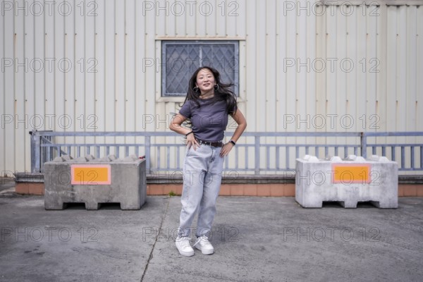 Female asian young K-pop dancer jumping hand on hip performing a choreography in an urban