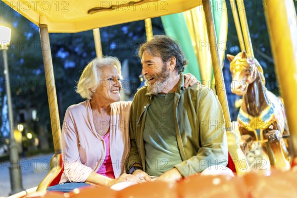 Happy senior friends sitting together in an old fashion carousel illuminated by light at night in
