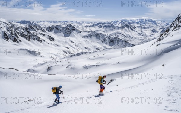 Two ski tourers in mountain landscape with snow, mountain panorama with summit of the Grisons Alps,