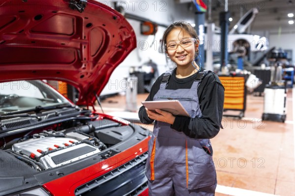 Confident female mechanic using a digital tablet, inspecting a car engine in a professional auto